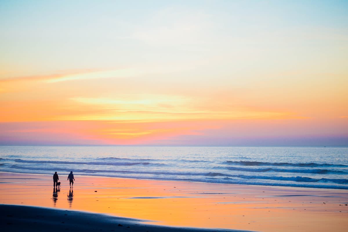 Two people walking on the beach under a pastel sunset