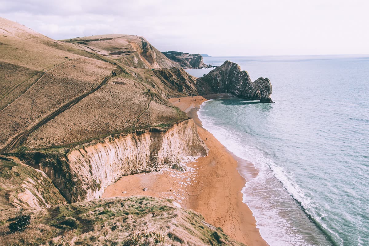 Aerial view of a curving sandy beach beneath chalk cliffs and green headlands