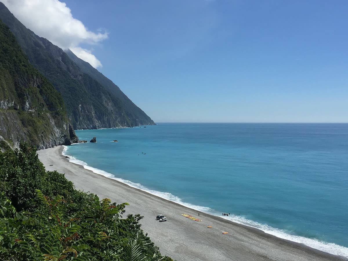 A coastal road winding along steep green cliffs above a turquoise sea